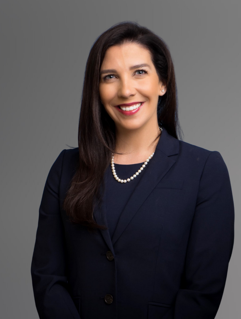 Attorney & Partner Sally M. Prieto-Chomat wearing a navy suit with white pearls