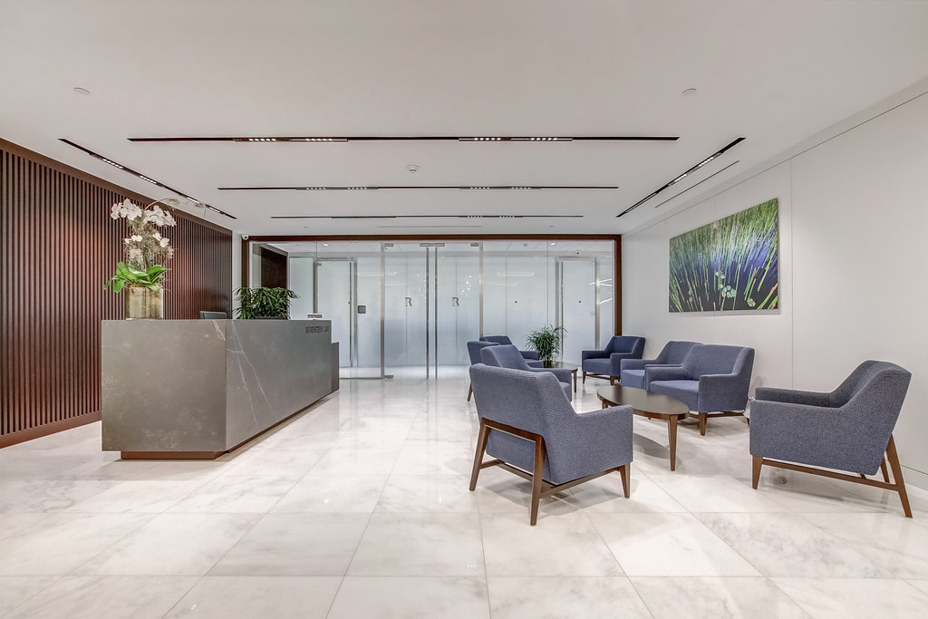 An empty Rubenstein Law Miami office lobby, blue chairs, wood paneling, marble floors and granite desk with white flowers. 